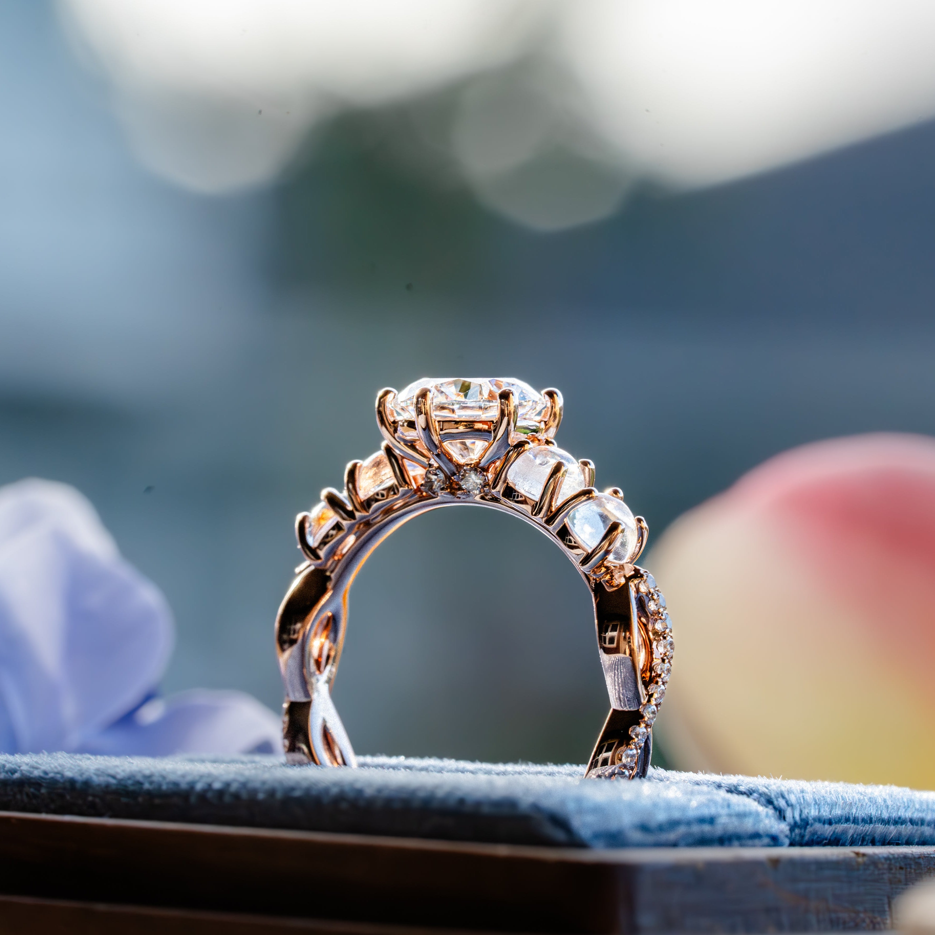 Rose gold ring with multiple diamonds and moonstones on a blue stand against a blurred natural background