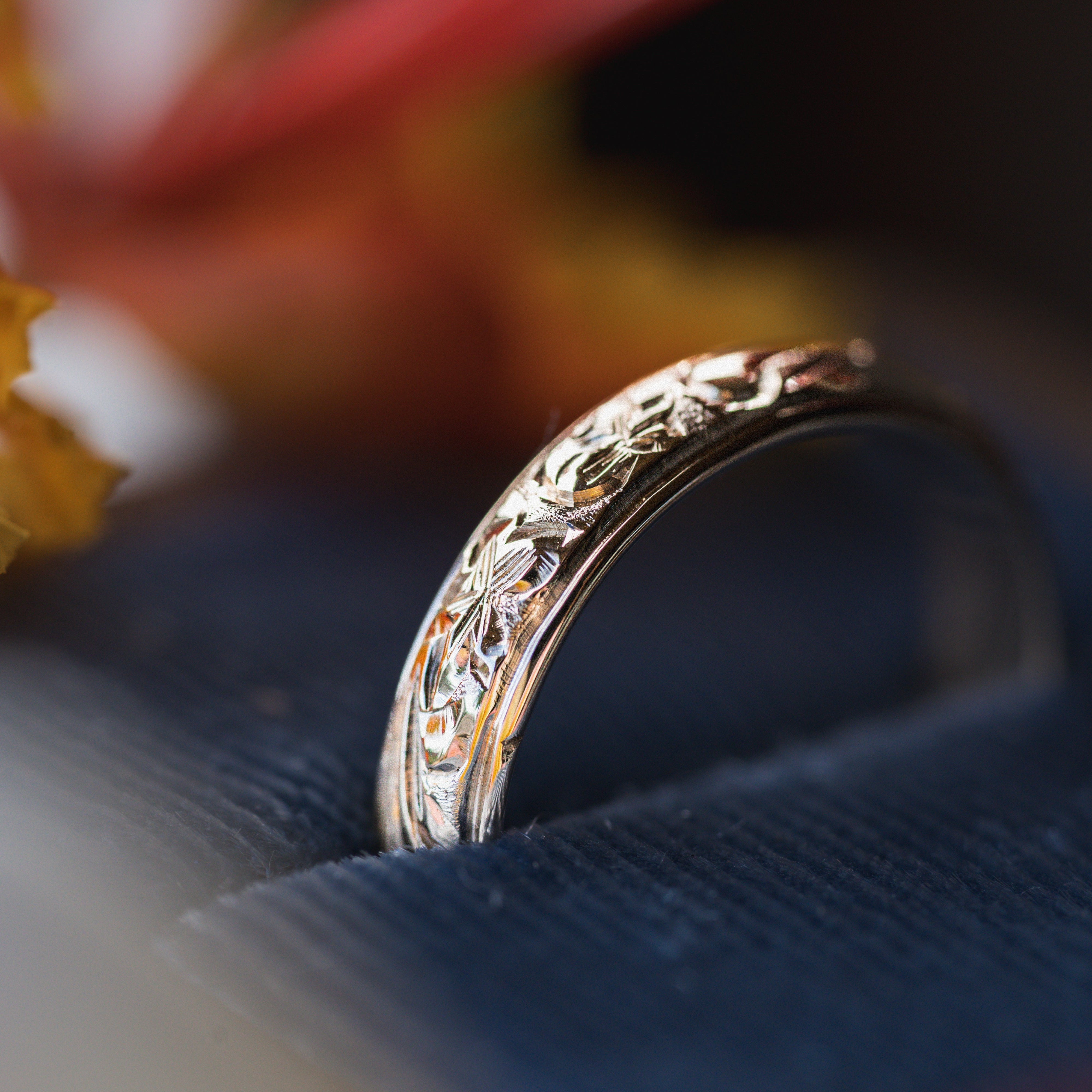 Gold ring with intricate hawaiian heirloom design on a textured surface with blurred floral background