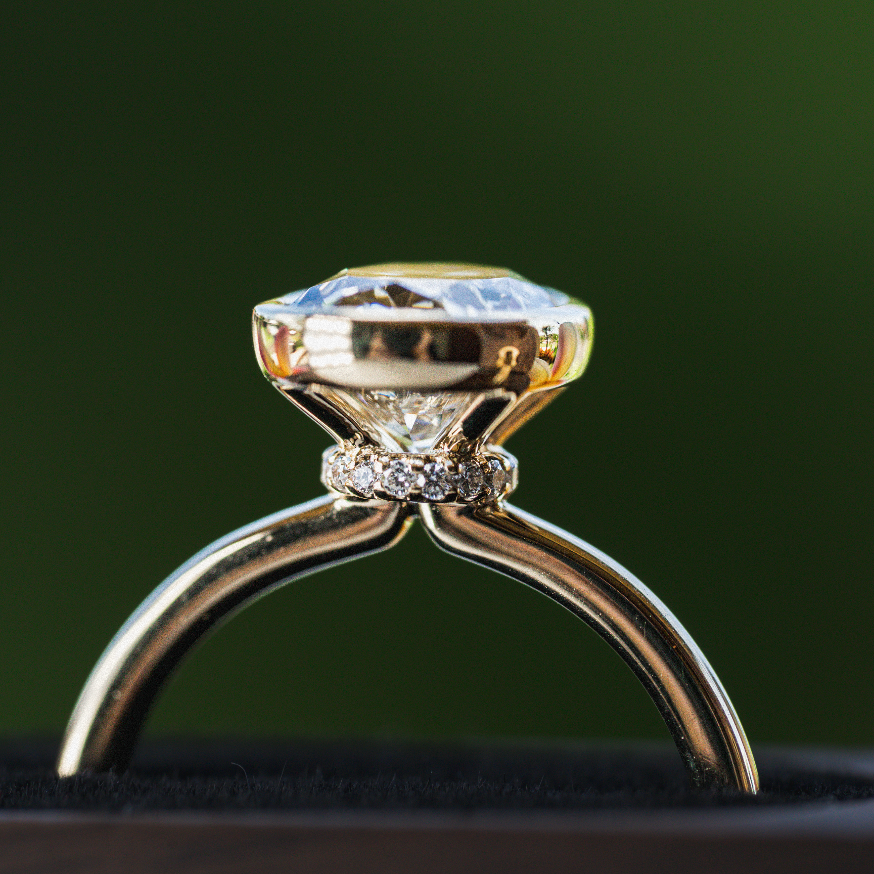 18k Gold ring with a bezel set oval diamond on a dark background with diamond collar
