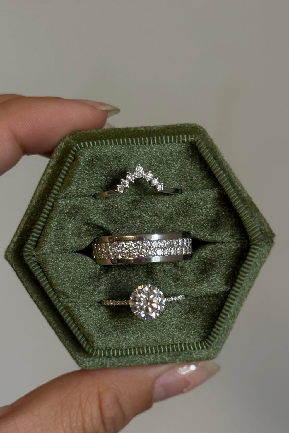 Hexagonal green jewelry box with three rings held by a hand against a neutral background