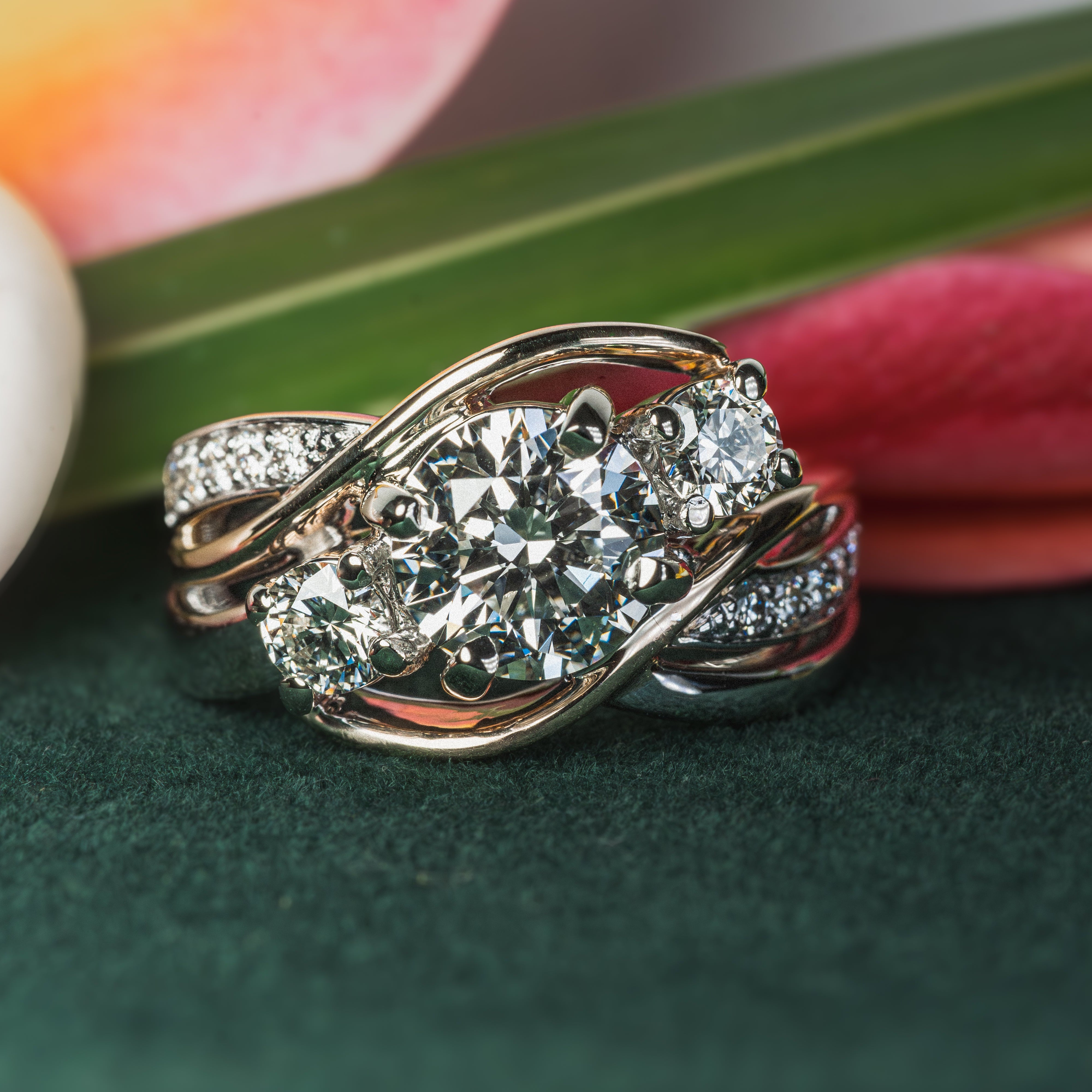 Gold ring with diamonds on a green surface with flowers in the background