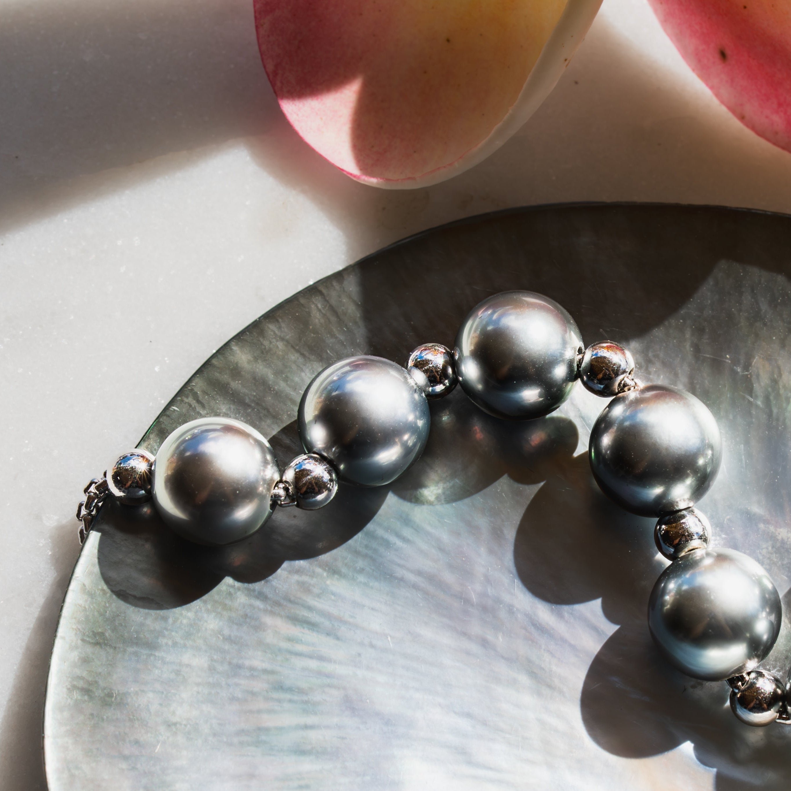 White gold beaded Tahitian pearl necklace on a shell with pink flowers in the background