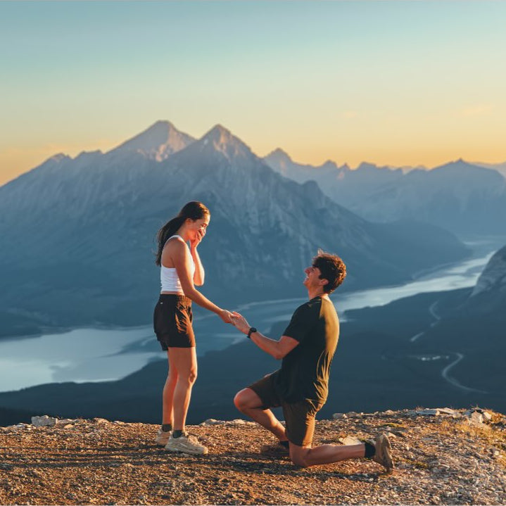 Man on one knee proposing to a woman with mountains and lake in the background