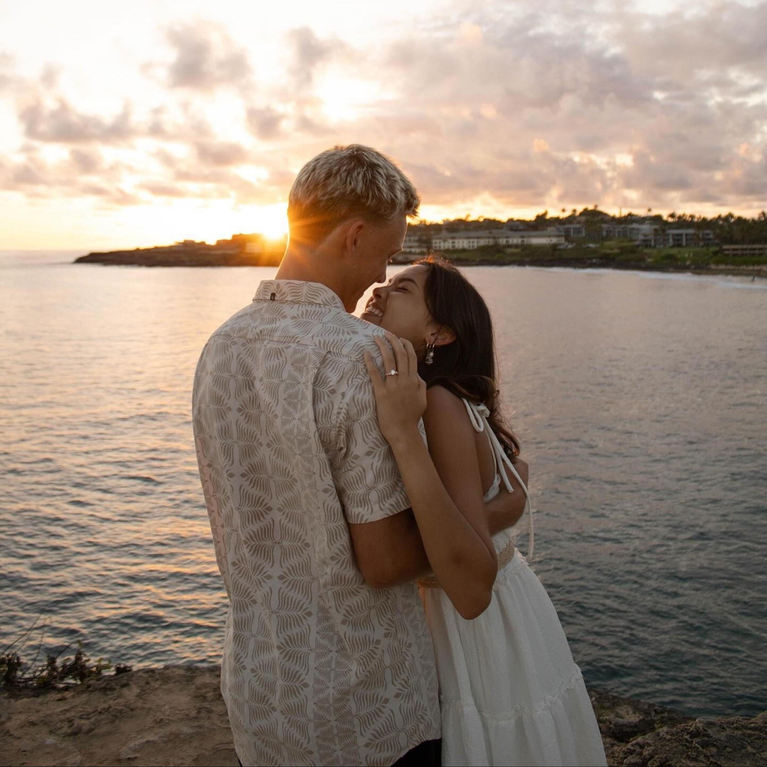 Couple embracing by a body of water with a sunset in the background